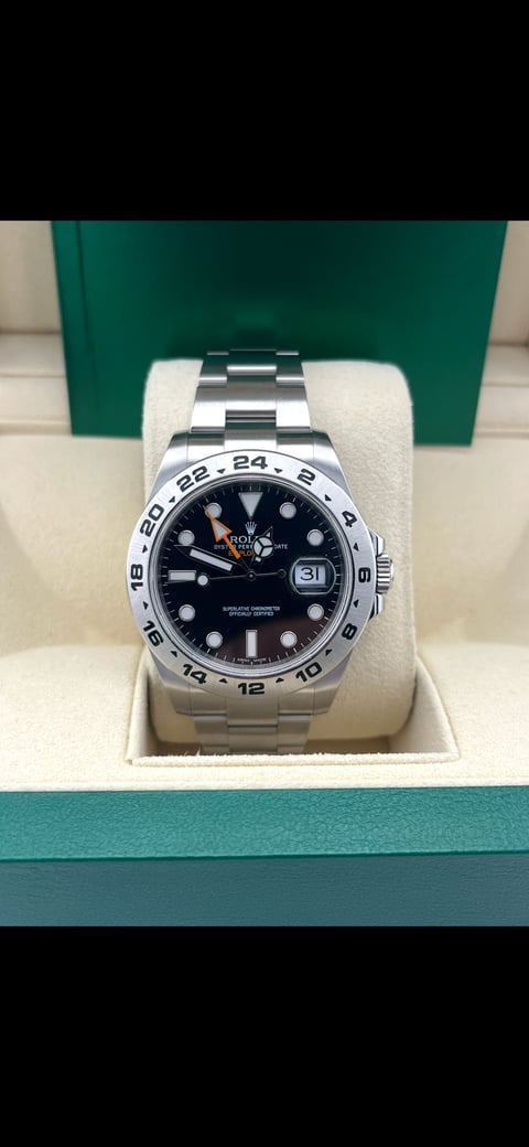 Silver Rolex sports watch with black dial and GMT bezel displayed on white cushion in green luxury gift box