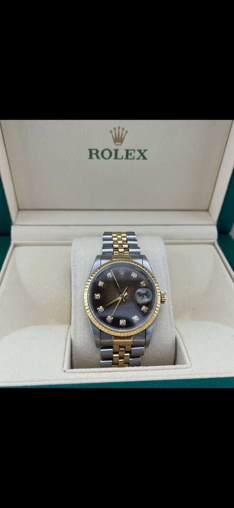Rolex watch with two-tone steel and gold bracelet, black diamond dial, and date window, displayed in official Rolex box