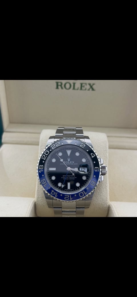 Rolex luxury watch with black dial and blue GMT bezel displayed on white pillow in branded box