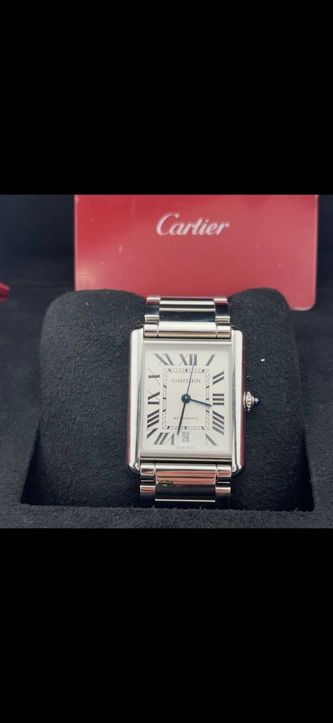 Cartier luxury watch with rectangular silver case and Roman numeral dial, displayed on black velvet holder with red Cartier box in background
