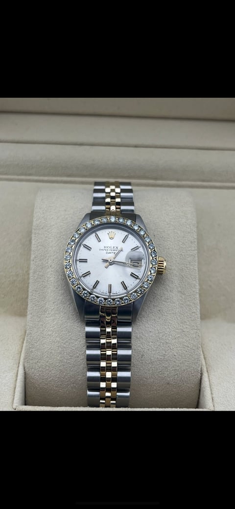 Luxury two-tone stainless steel and gold Rolex watch with diamond bezel and white dial on beige watch roll display